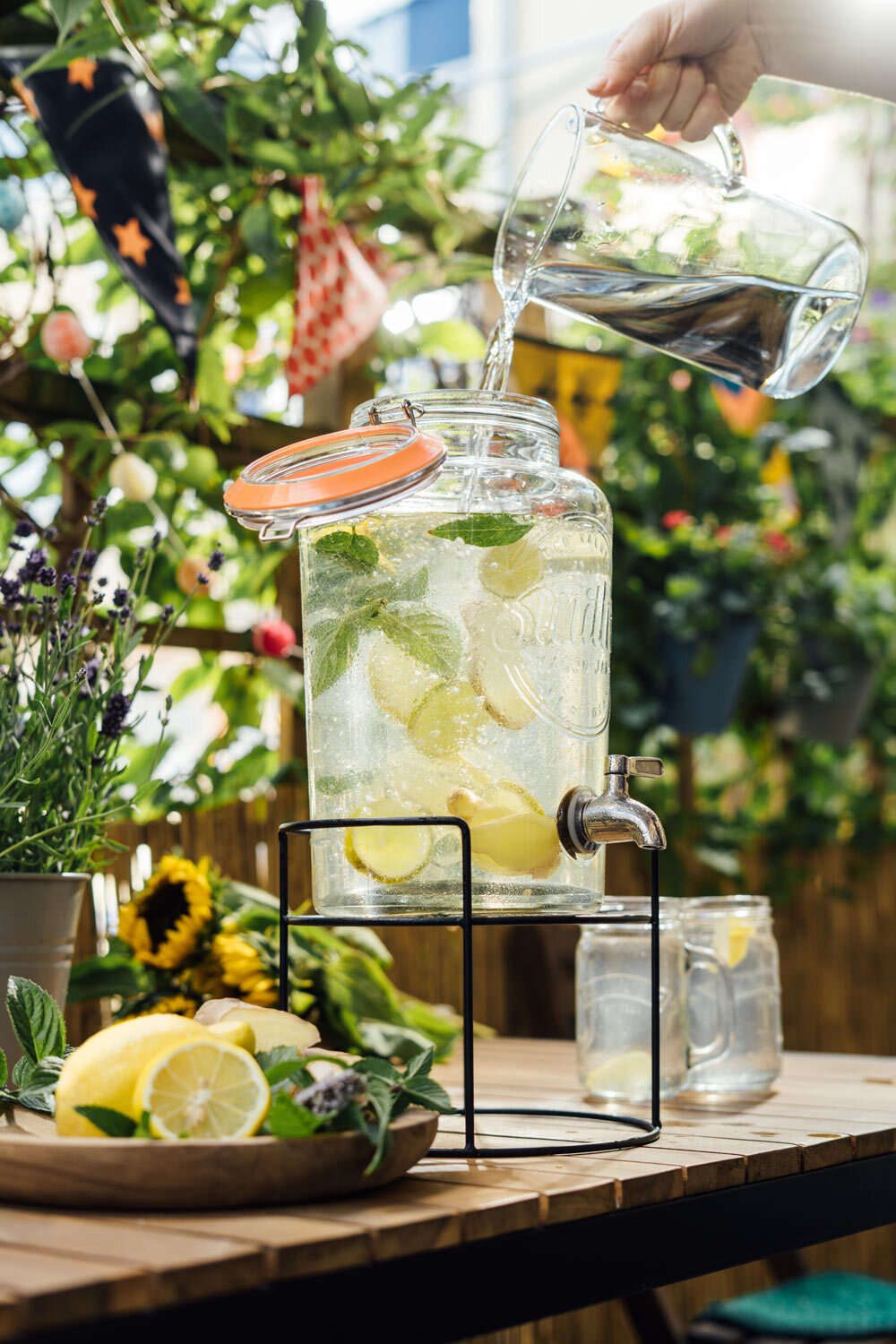 Wasser wird in einen Getränkespender mit Zitronen und Minze gegossen, selbst gemachte Limonade auf dem Balkon