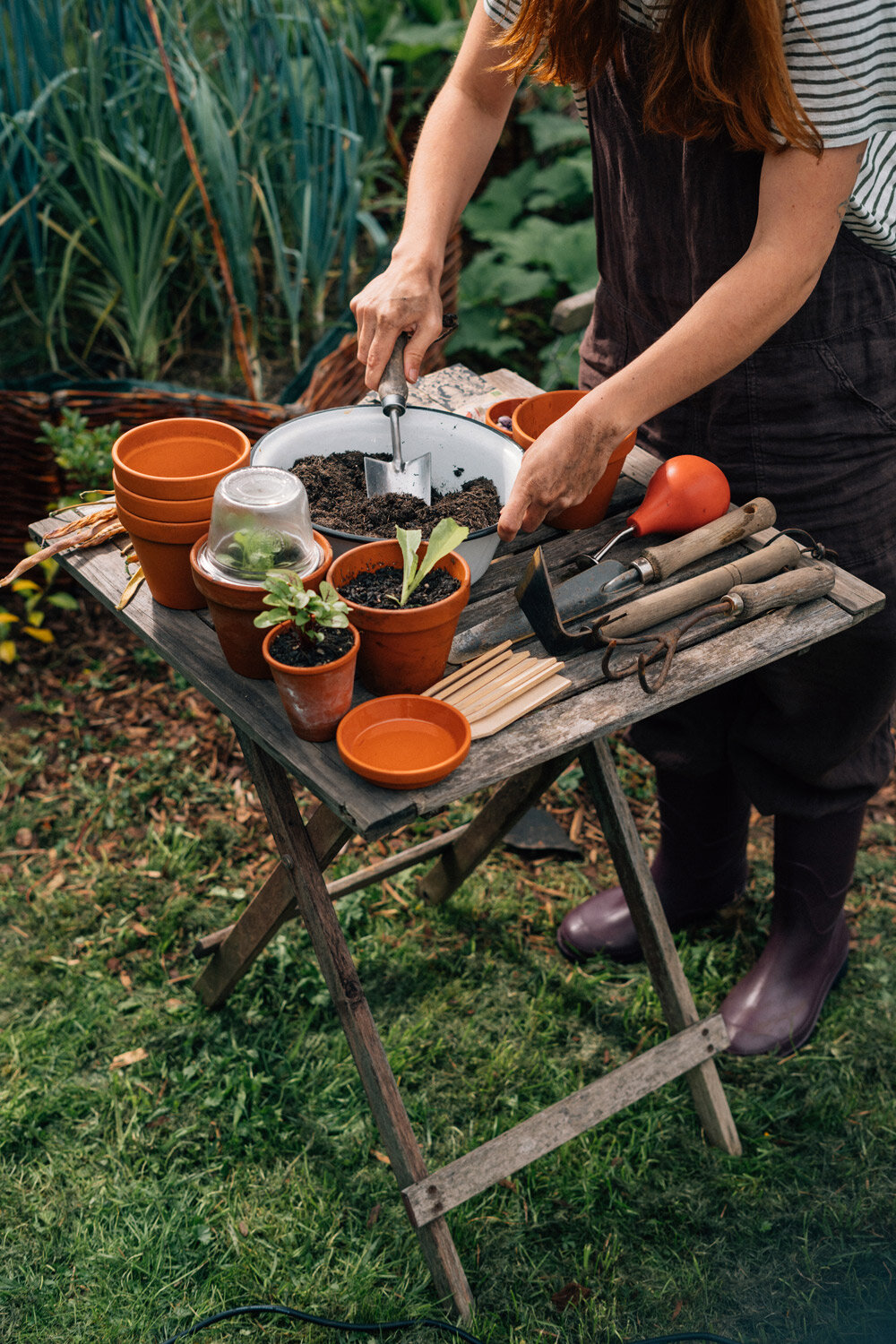 Gärtnerin füllt am Gartentisch Erde in kleine Tontöpfe für die Aussaat